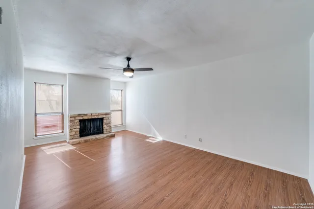 an empty room with wooden floor fireplace and windows
