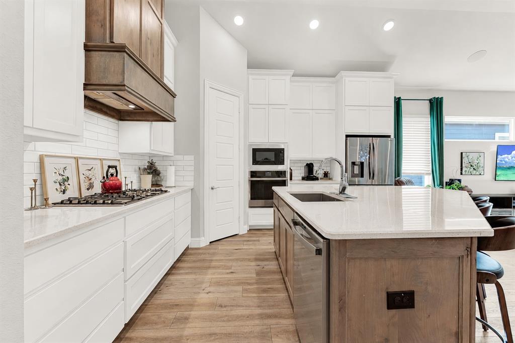 6404 Trezevant Street Rowlett, TX 75089 - Photo 7 of 30 Modern kitchen featuring a gas cooktop with a custom wood-finish range hood, white subway tile backsplash, and light-toned countertops