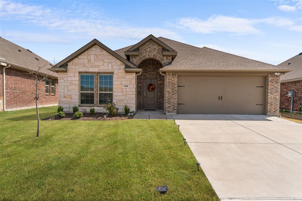 View of front facade featuring a front yard, a shingled roof, concrete driveway, a garage, and brick siding