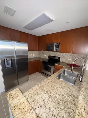 a kitchen with stainless steel appliances kitchen island granite countertop a refrigerator and a sink