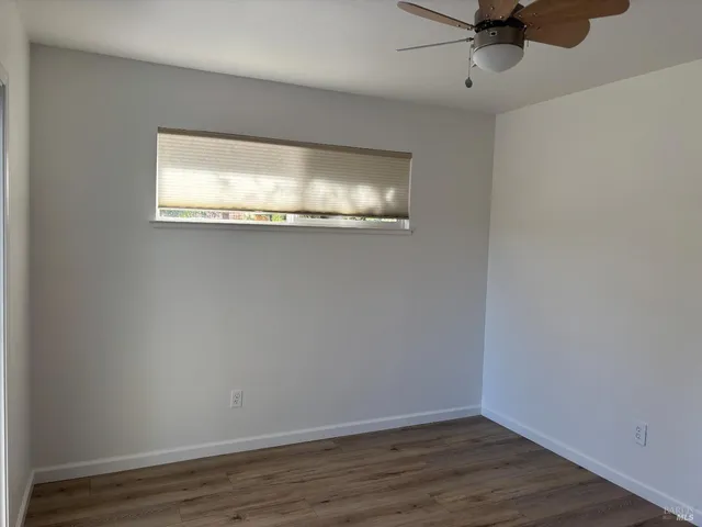 an empty room with wooden floor fan and windows