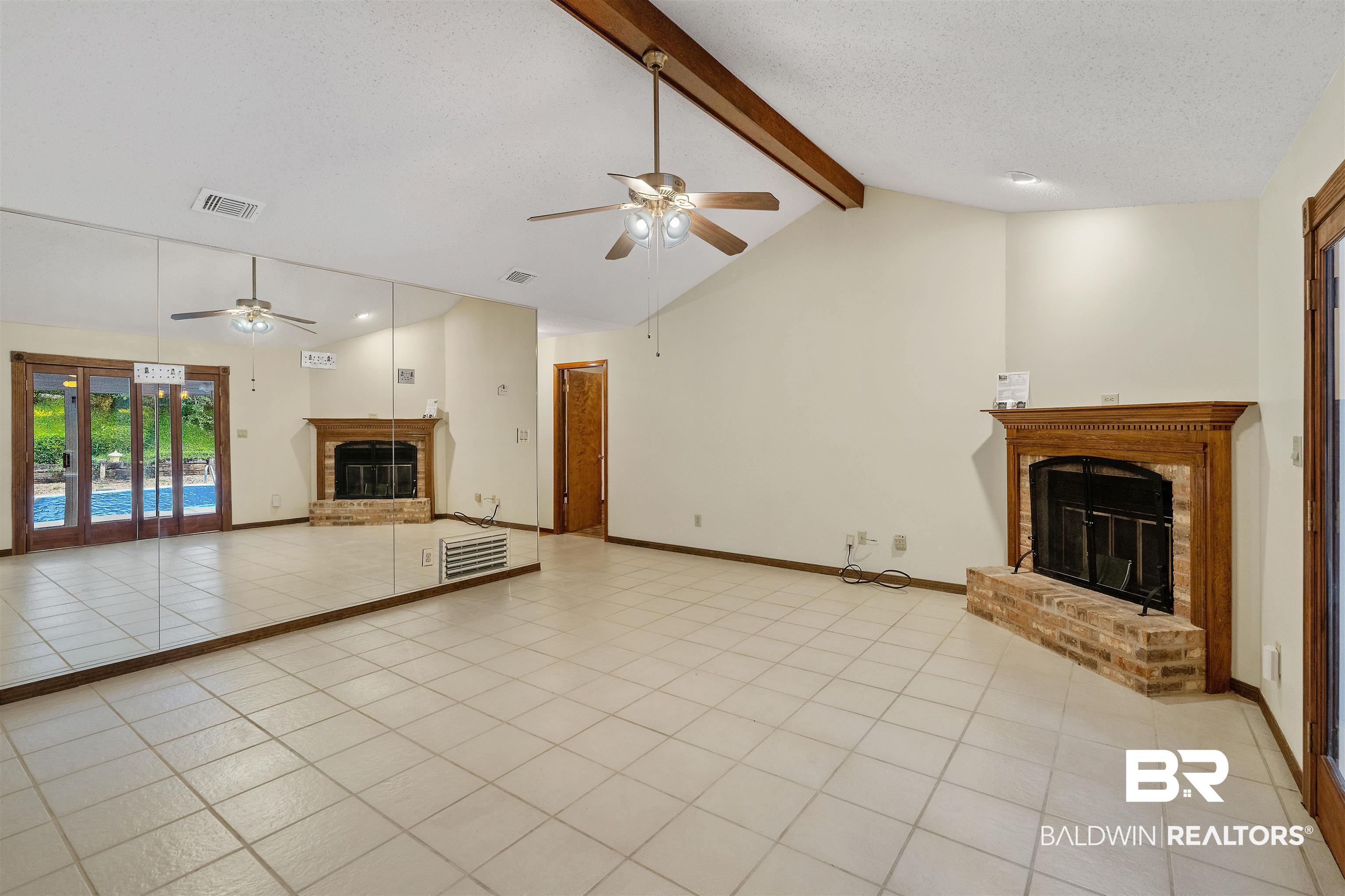 438 Ridgewood Drive Daphne, AL 36526 - Photo 8 of 28 Unfurnished living room with lofted ceiling with beams, a brick fireplace, ceiling fan, and light tile patterned floors