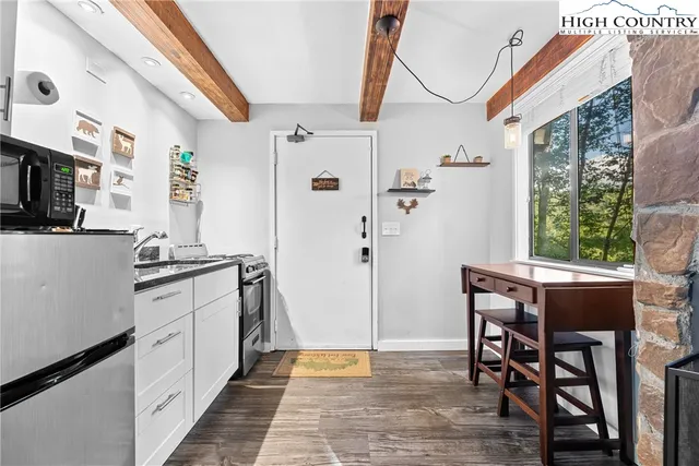 a kitchen with stainless steel appliances granite countertop a dining table chairs a microwave and a view of living room