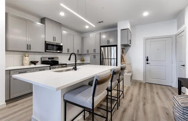 a kitchen with stainless steel appliances a sink a stove a refrigerator with white cabinets and wooden floor