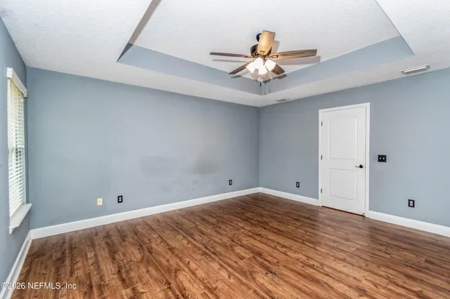 an empty room with wooden floor fan and windows