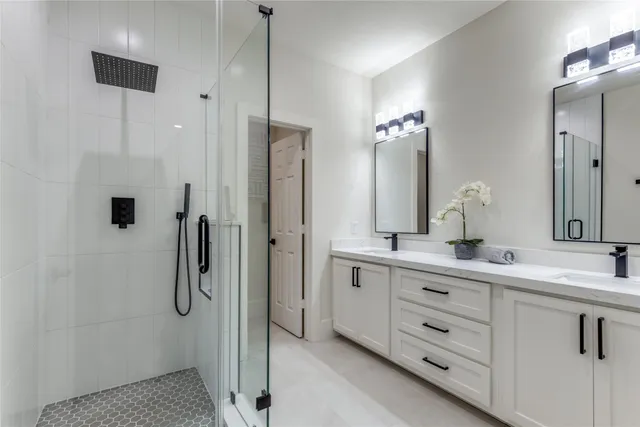 a bathroom with a double vanity sink a mirror a glass door a shower and a mirror