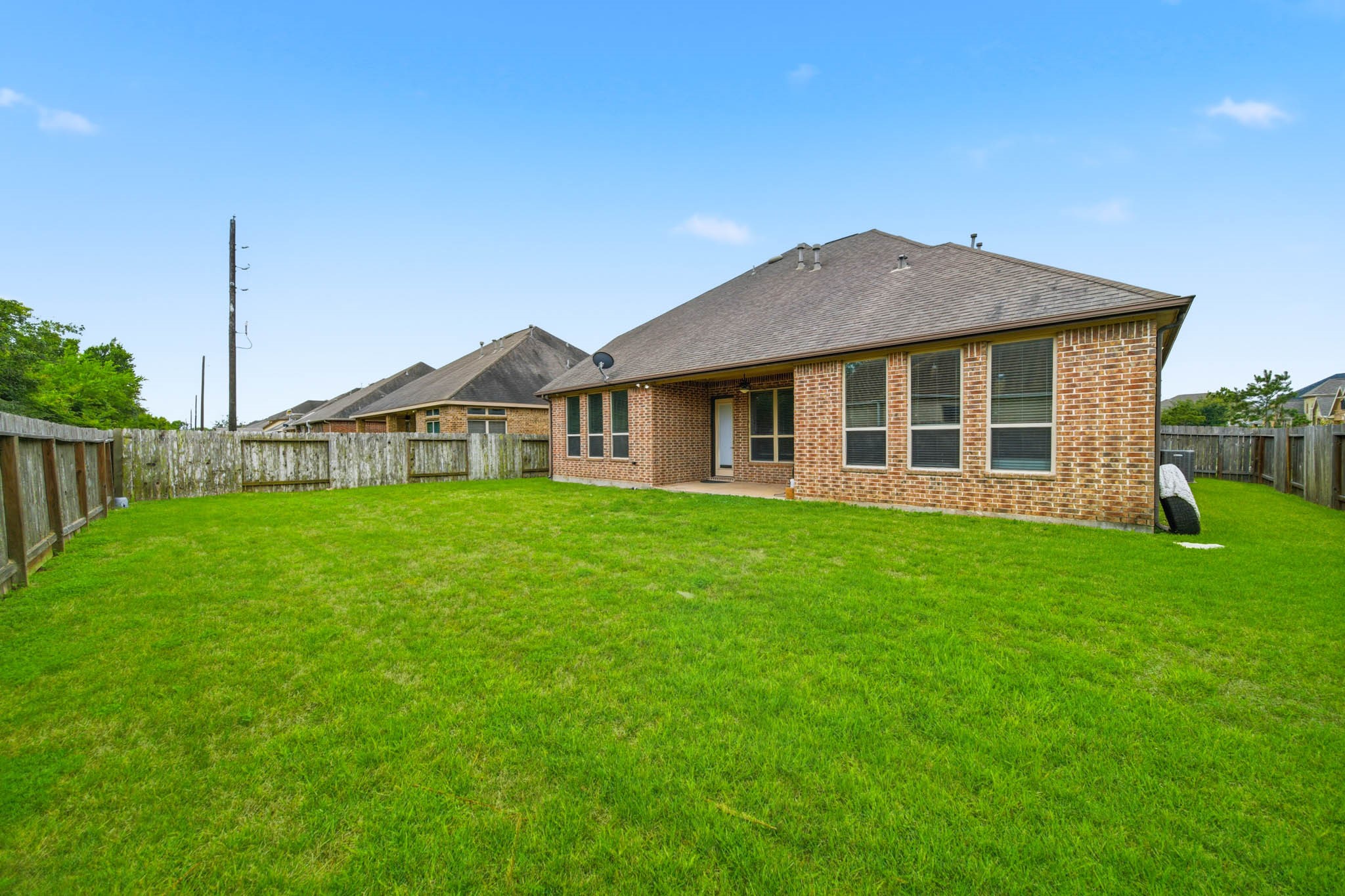 5303 Mesquite Willow Lane Rosharon, TX 77583 - Photo 30 of 32 This photo showcases a spacious backyard with well-maintained grass and a brick exterior home. The area is fenced, providing privacy, and features multiple large windows and a covered patio. Ideal for outdoor activities and relaxation.