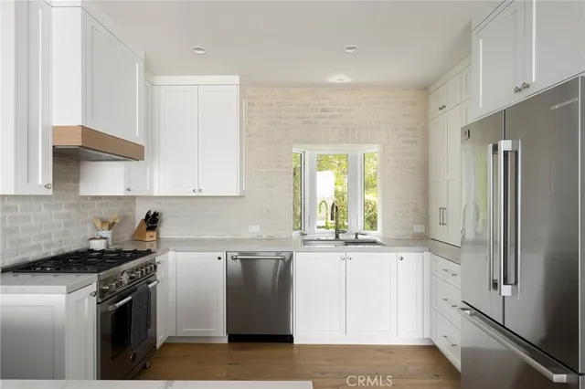a kitchen with stainless steel appliances granite countertop a refrigerator a sink and white cabinets