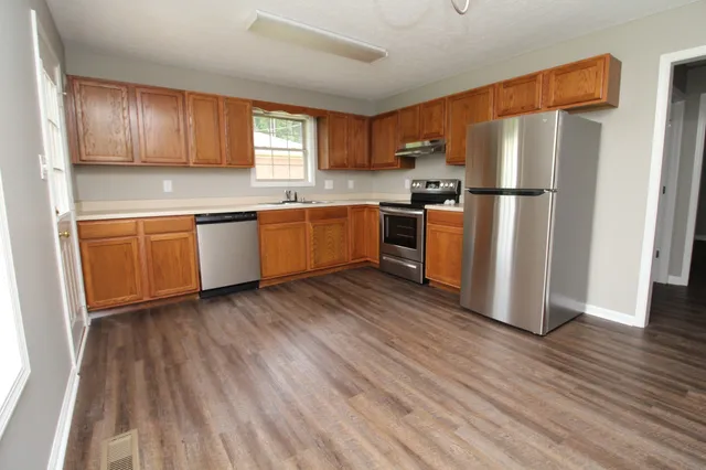 a kitchen with granite countertop wooden floors stainless steel appliances a sink and a window