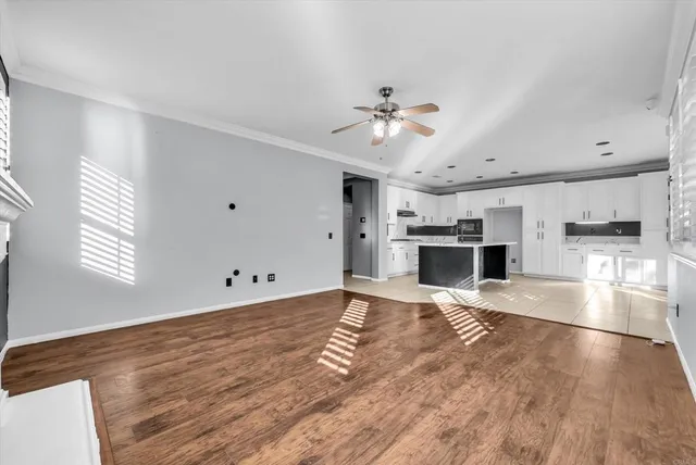 a view of empty room with wooden floor and kitchen view