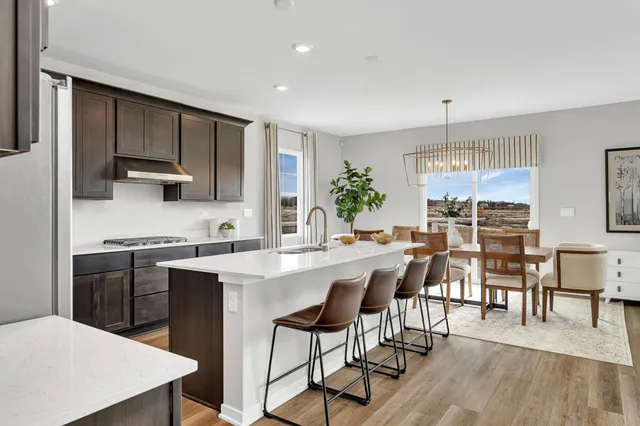 a kitchen with stainless steel appliances granite countertop a stove a refrigerator a kitchen island a dining table and chairs with wooden floor