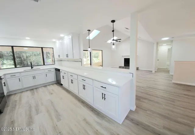 a large white kitchen with a large island wooden floor and stainless steel appliances