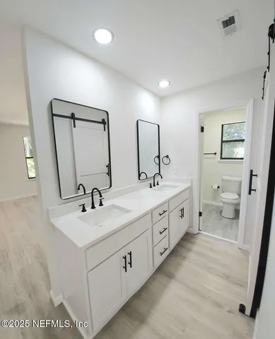 a spacious bathroom with double vanity sink a mirror and a toilet
