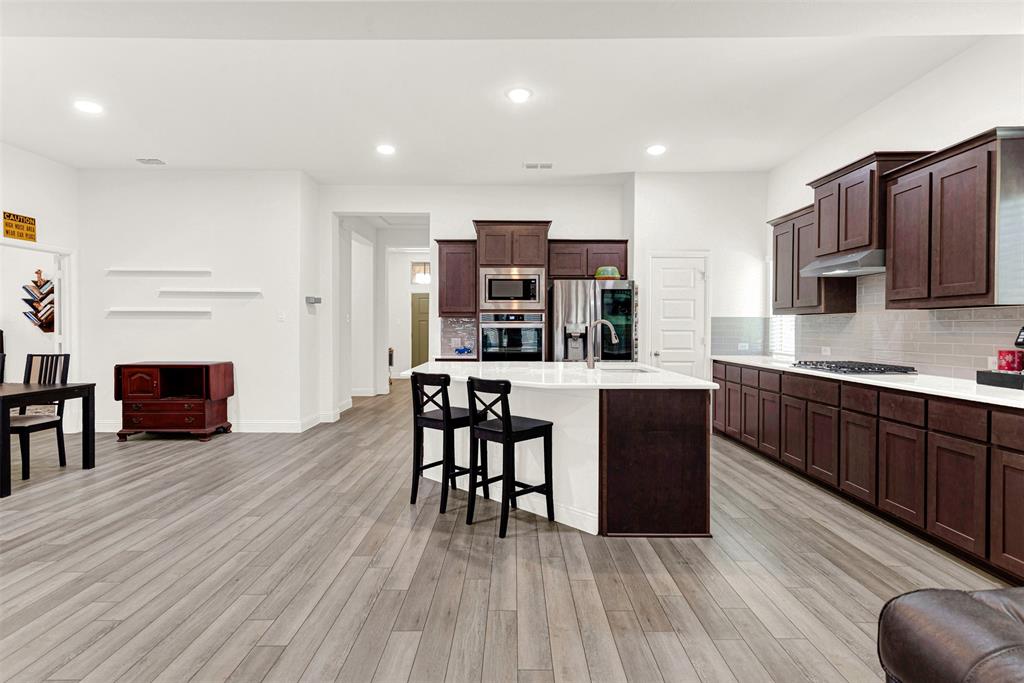 817 Amy Boulevard Anna, TX 75409 - Photo 10 of 40 a kitchen with stainless steel appliances granite countertop a refrigerator a stove top oven and a dining table with wooden floor
