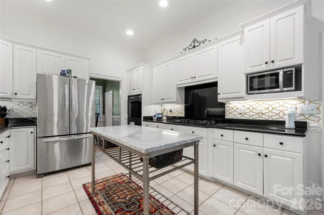 a open kitchen with granite countertop a stove a sink dishwasher a dining table and chairs with white cabinets
