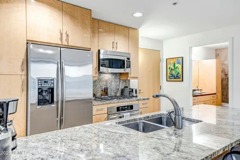 a kitchen with stainless steel appliances granite countertop a refrigerator a stove and a sink with wooden floor