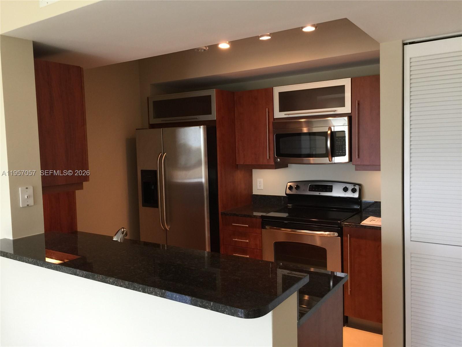 7350 Southwest 89th Street, Unit 1611S Miami, FL 33156 - Photo 4 of 16 a kitchen with stainless steel appliances granite countertop a refrigerator a stove and a sink with wooden floor