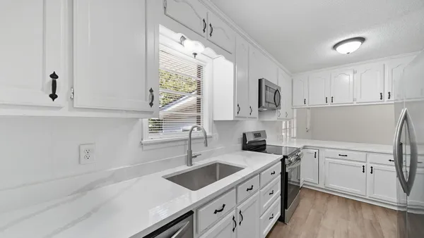 a kitchen with a sink dishwasher a stove and white cabinets with wooden floor