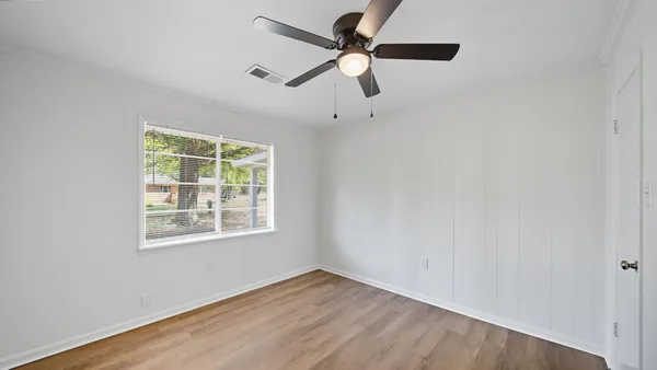an empty room with wooden floor fan and windows