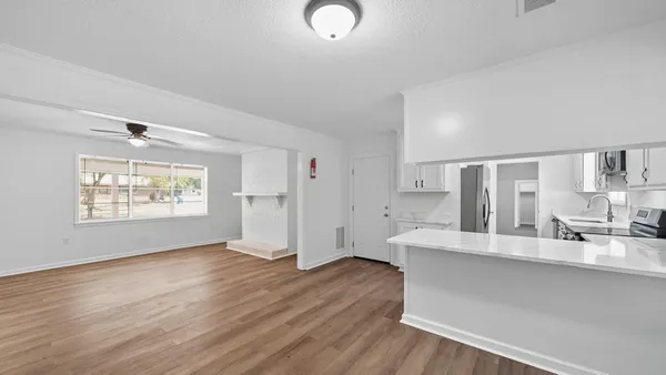 a large white kitchen with stainless steel appliances granite countertop a dishwasher a stove a refrigerator with white cabinets and wooden floor