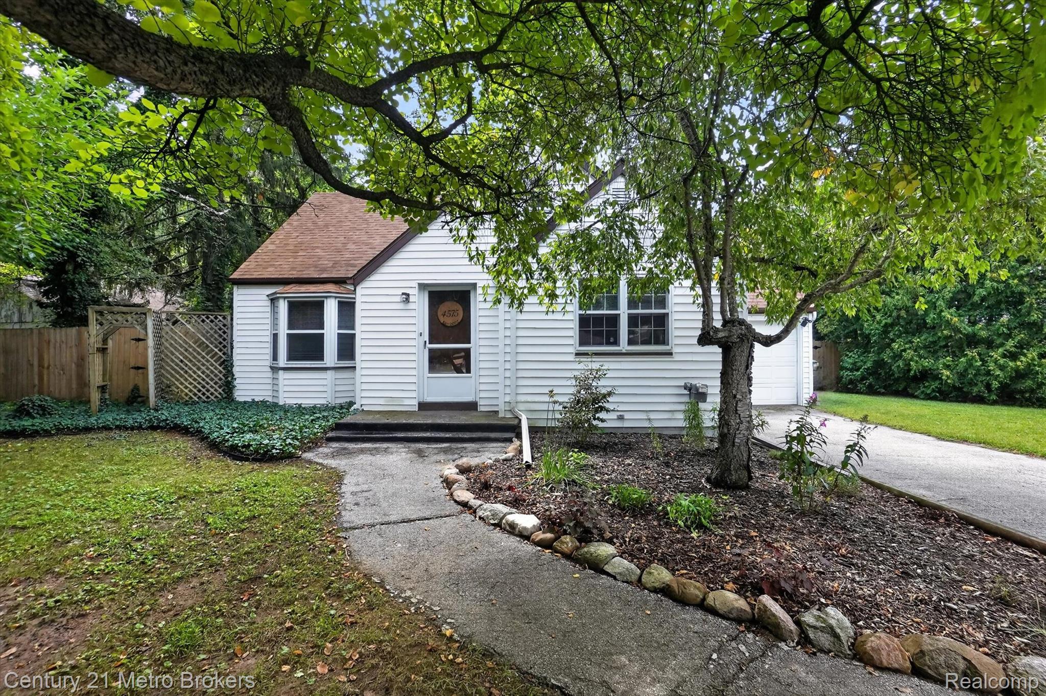 4575 Brockway Road Saginaw, MI 48638 - Photo 4 of 44 White siding exterior with a brown shingle roof, accompanied by a paved walkway and mature trees