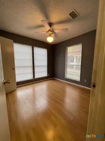 an empty room with wooden floor fan and windows