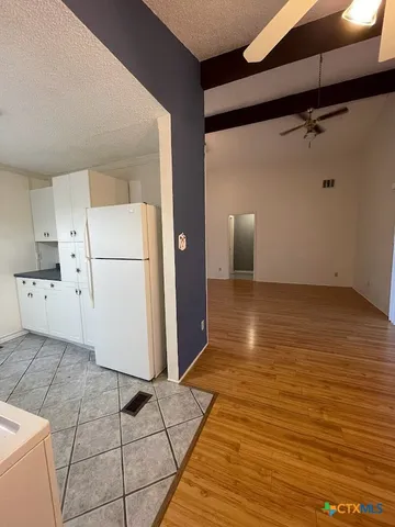 a view of a refrigerator in kitchen and an empty room with wooden floor