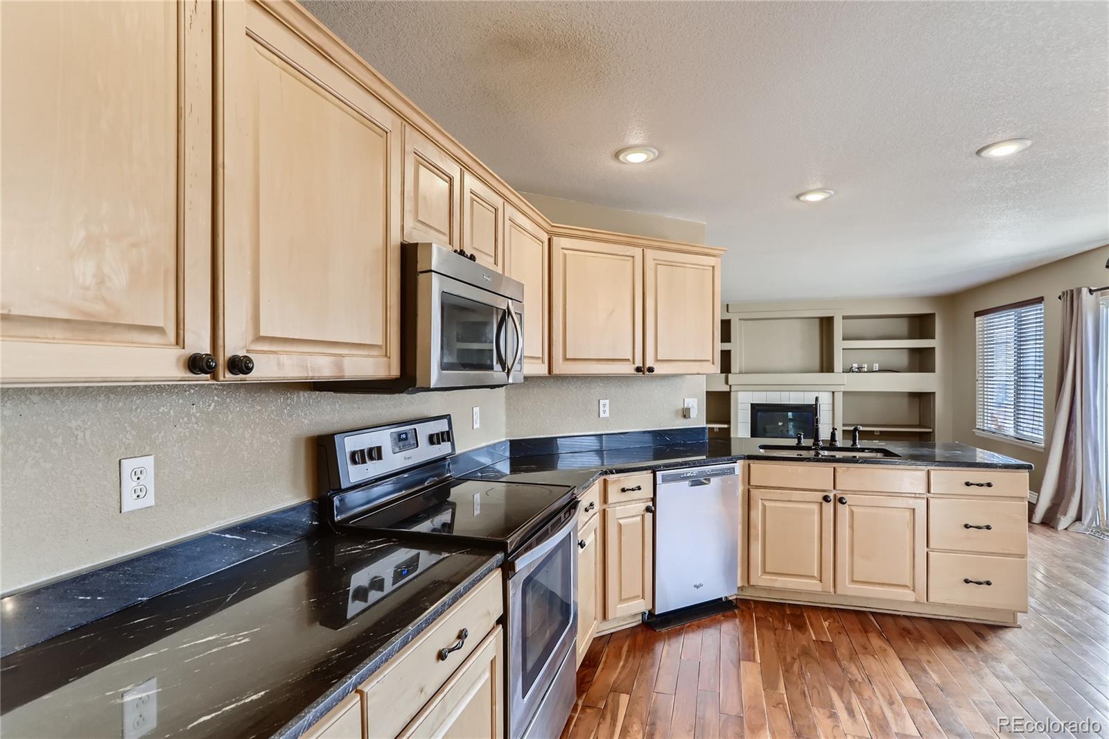 3905 South Kirk Way Aurora, CO 80013 - Photo 7 of 33 a kitchen with stainless steel appliances granite countertop a stove a sink and white cabinets with wooden floor