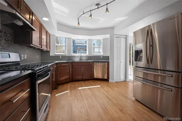 a kitchen with stainless steel appliances granite countertop a refrigerator a sink dishwasher a stove and white countertops with wooden floor