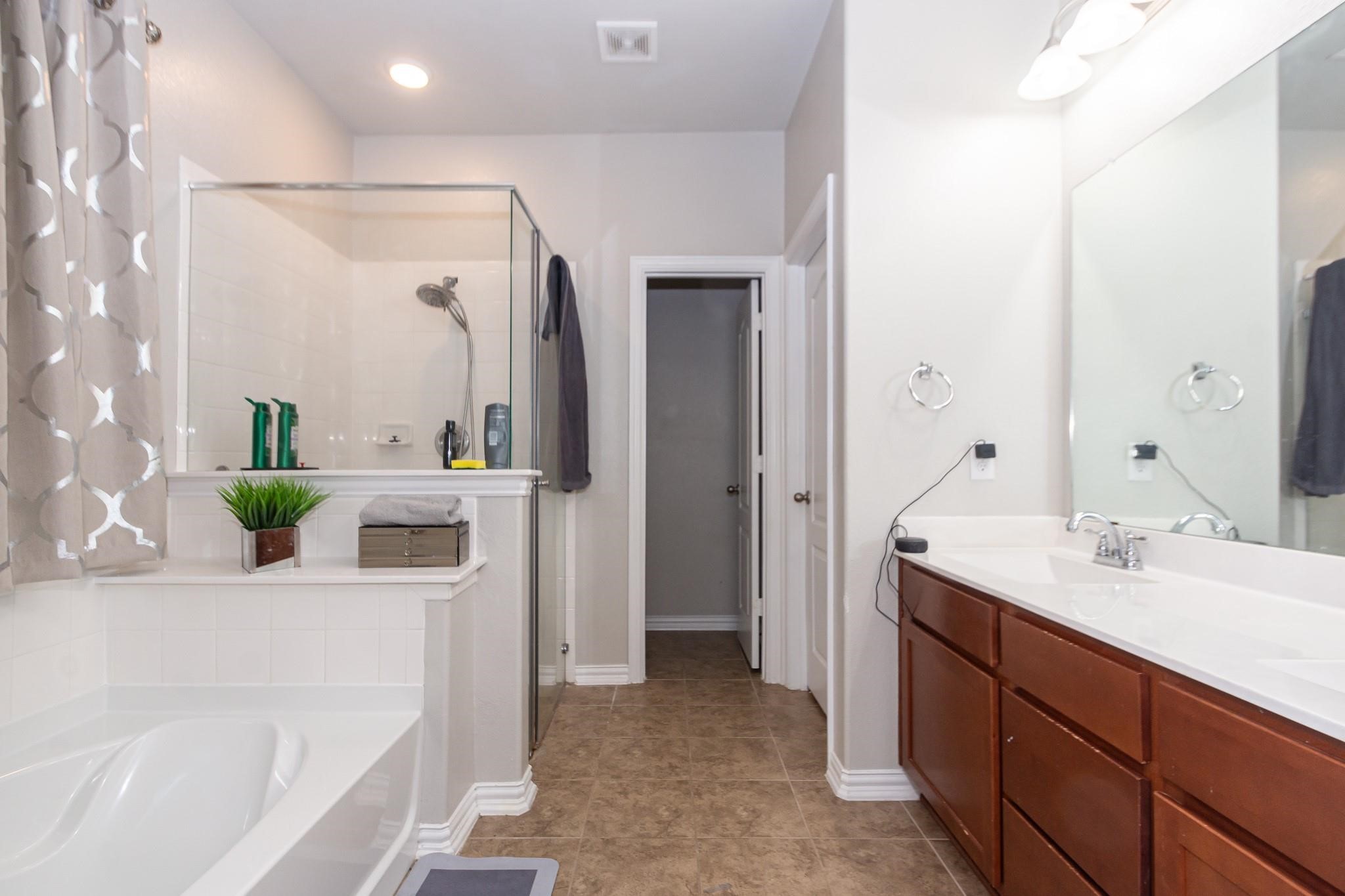 208 Timber Grove Court Clute, TX 77531 - Photo 13 of 22 This bathroom features a spacious layout with a glass-enclosed shower, a large bathtub, and a double-sink vanity. It has modern fixtures, ample counter space, and neutral tile flooring, creating a clean and inviting atmosphere.