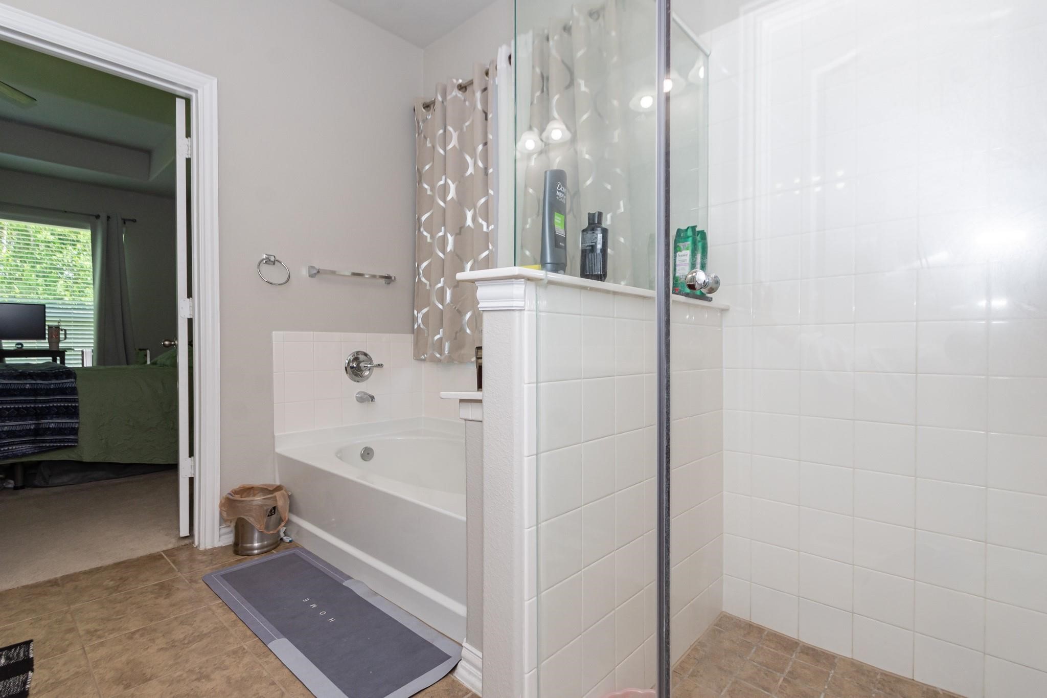208 Timber Grove Court Clute, TX 77531 - Photo 14 of 22 This bathroom features a spacious layout with a glass-enclosed shower and a separate bathtub. It has tiled flooring and a neutral color scheme, with a view into the adjacent bedroom through a doorway.