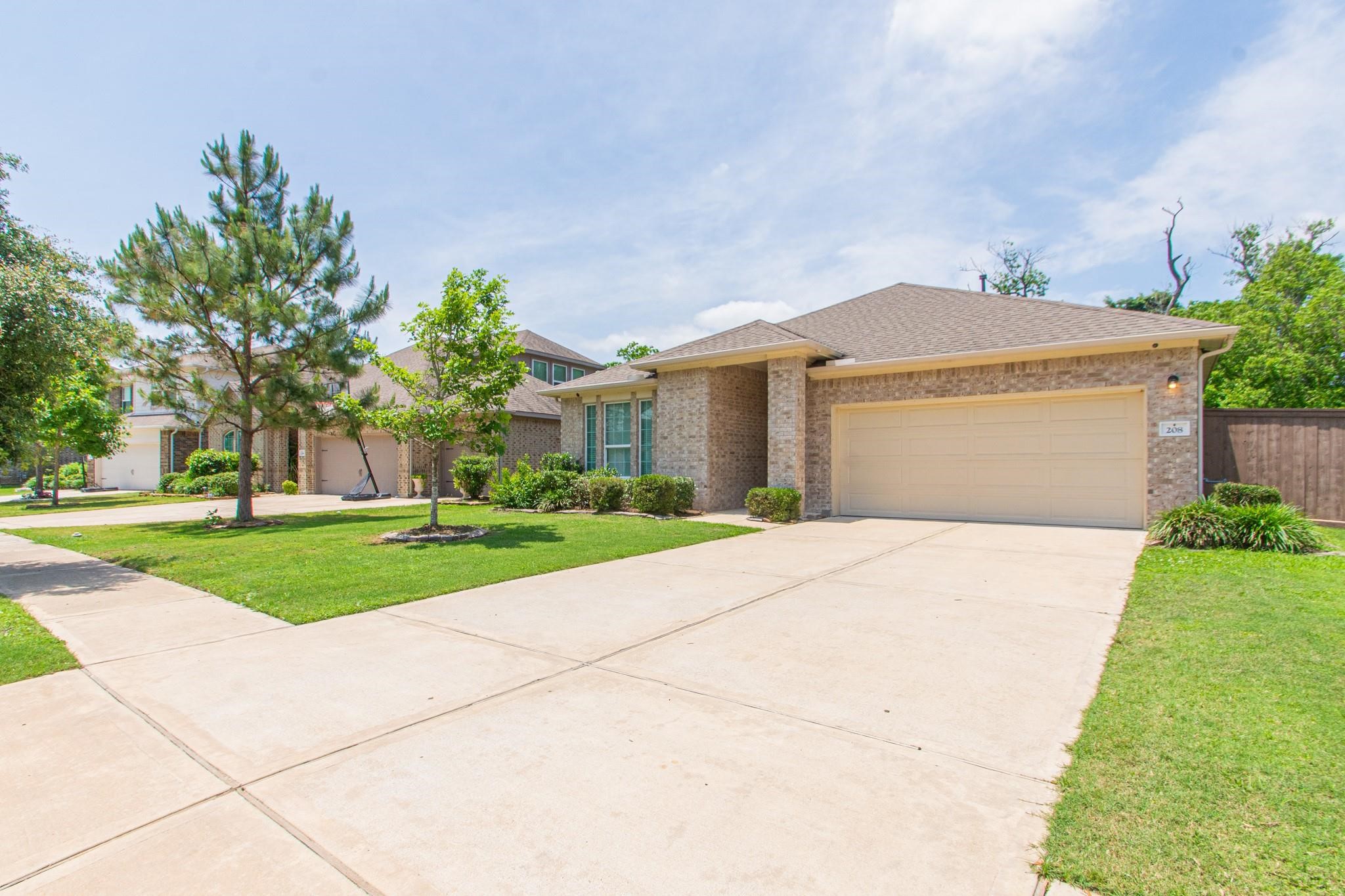 208 Timber Grove Court Clute, TX 77531 - Photo 2 of 22 This photo shows a single-story brick home with a well-maintained front yard, featuring a two-car garage and a spacious driveway. The neighborhood appears quiet and green with a sidewalk and trees lining the street.