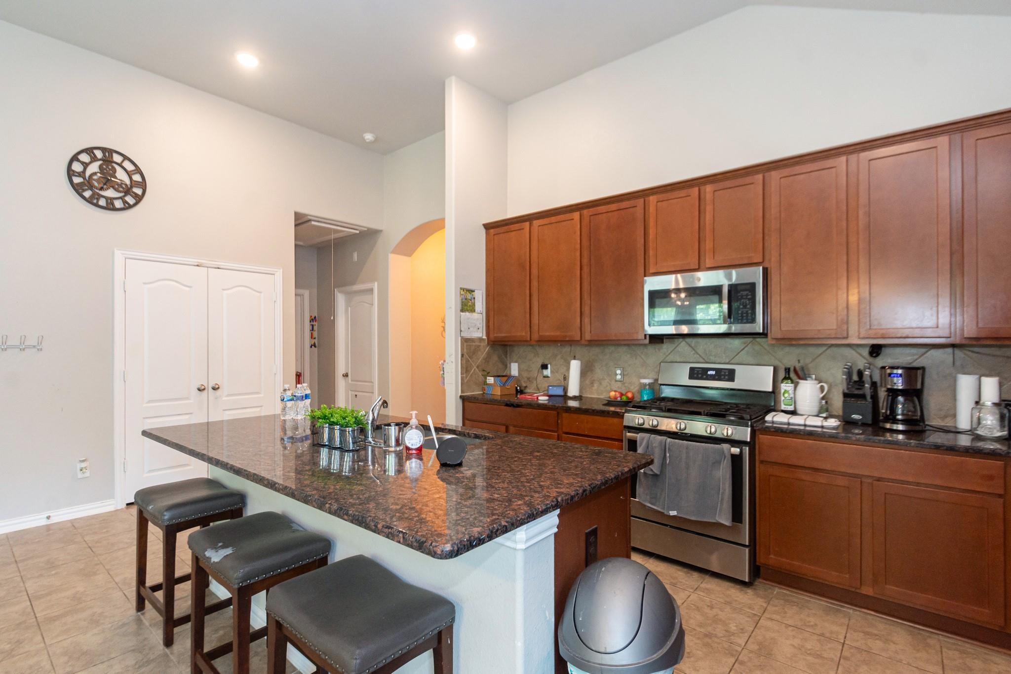 208 Timber Grove Court Clute, TX 77531 - Photo 6 of 22 Spacious kitchen with high ceilings, featuring a large granite island with seating, stainless steel appliances, and ample wooden cabinetry. The room is bright and functional, ideal for cooking and entertaining.
