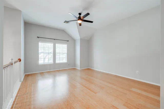 an empty room with wooden floor fan and windows