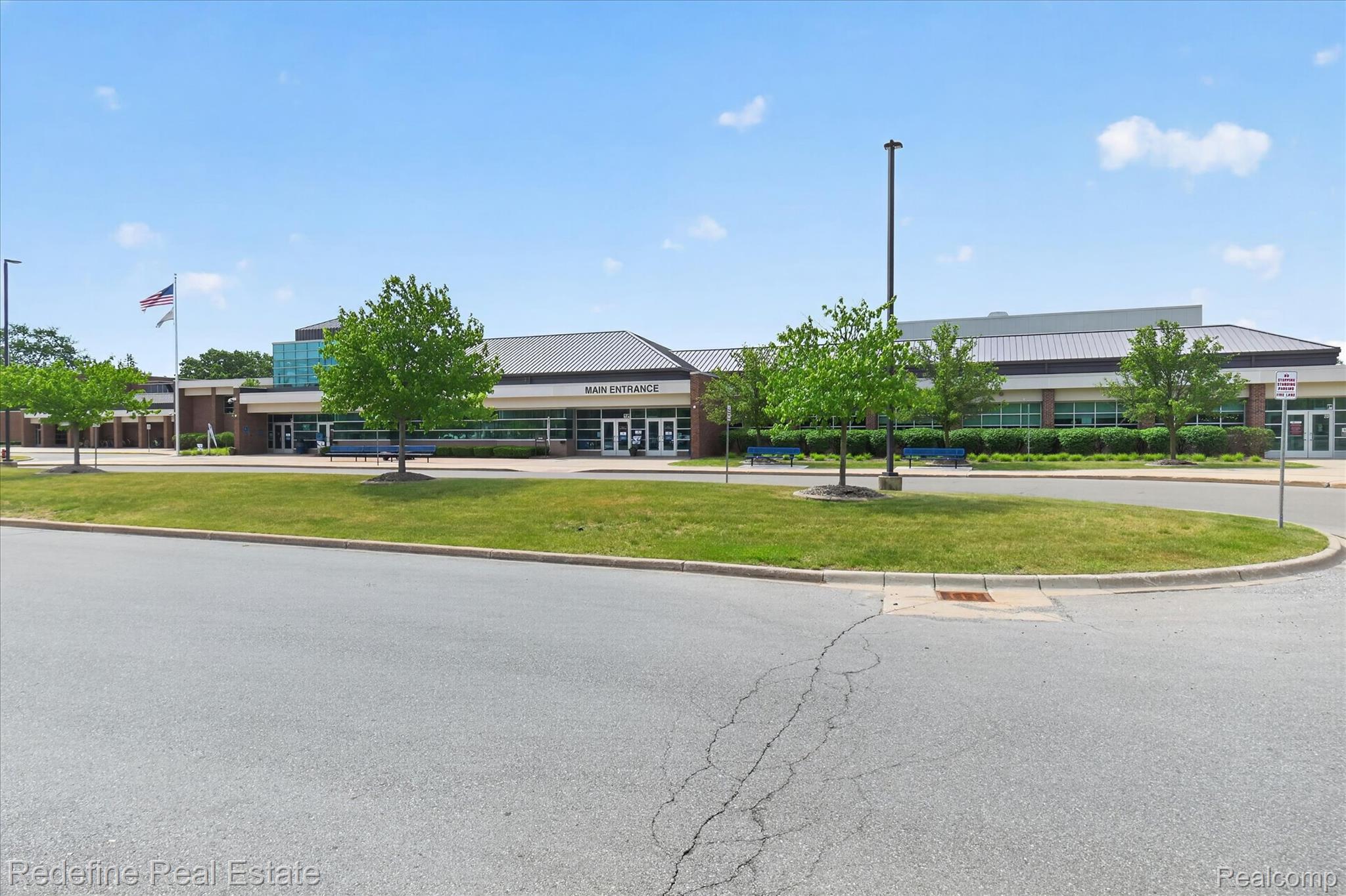 2976 Andlaur Drive Rochester, MI 48307 - Photo 58 of 60 Commercial building with a prominent "MAIN ENTRANCE" sign, extensive glass windows, a dark shingle roof, and a flagpole