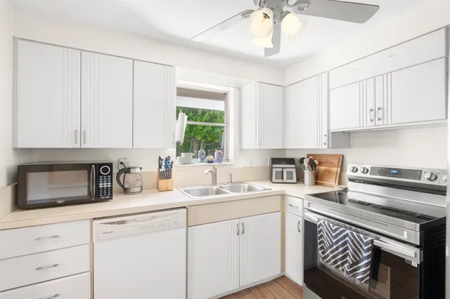 a kitchen with a sink dishwasher a stove and white cabinets with wooden floor