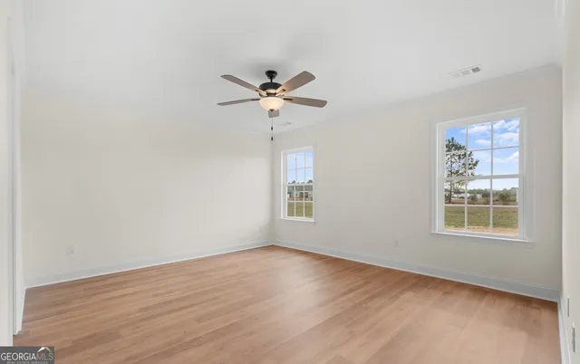 an empty room with wooden floor ceiling fan and window