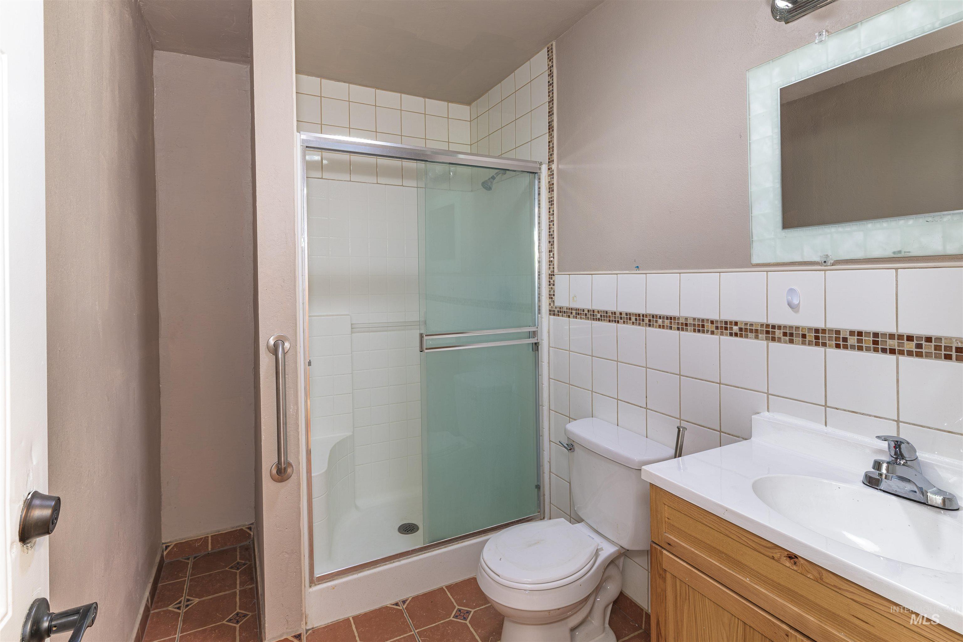2003 North Cole Road Boise, ID 83704 - Photo 15 of 40 Full bathroom featuring vanity, tile walls, a stall shower, and dark tile patterned flooring