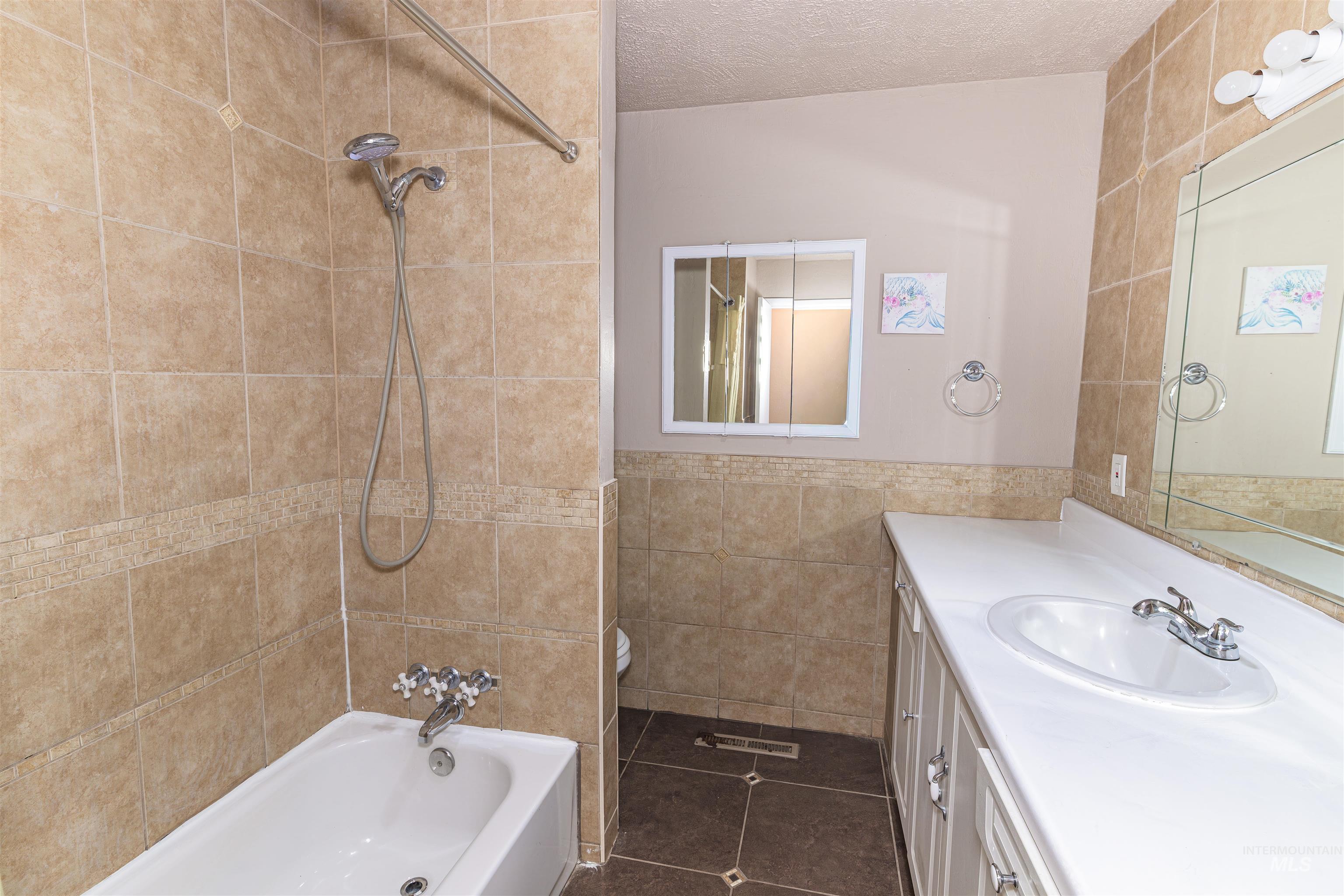 2003 North Cole Road Boise, ID 83704 - Photo 21 of 40 Bathroom featuring vanity, tile walls, washtub / shower combination, dark tile patterned flooring, and a textured ceiling