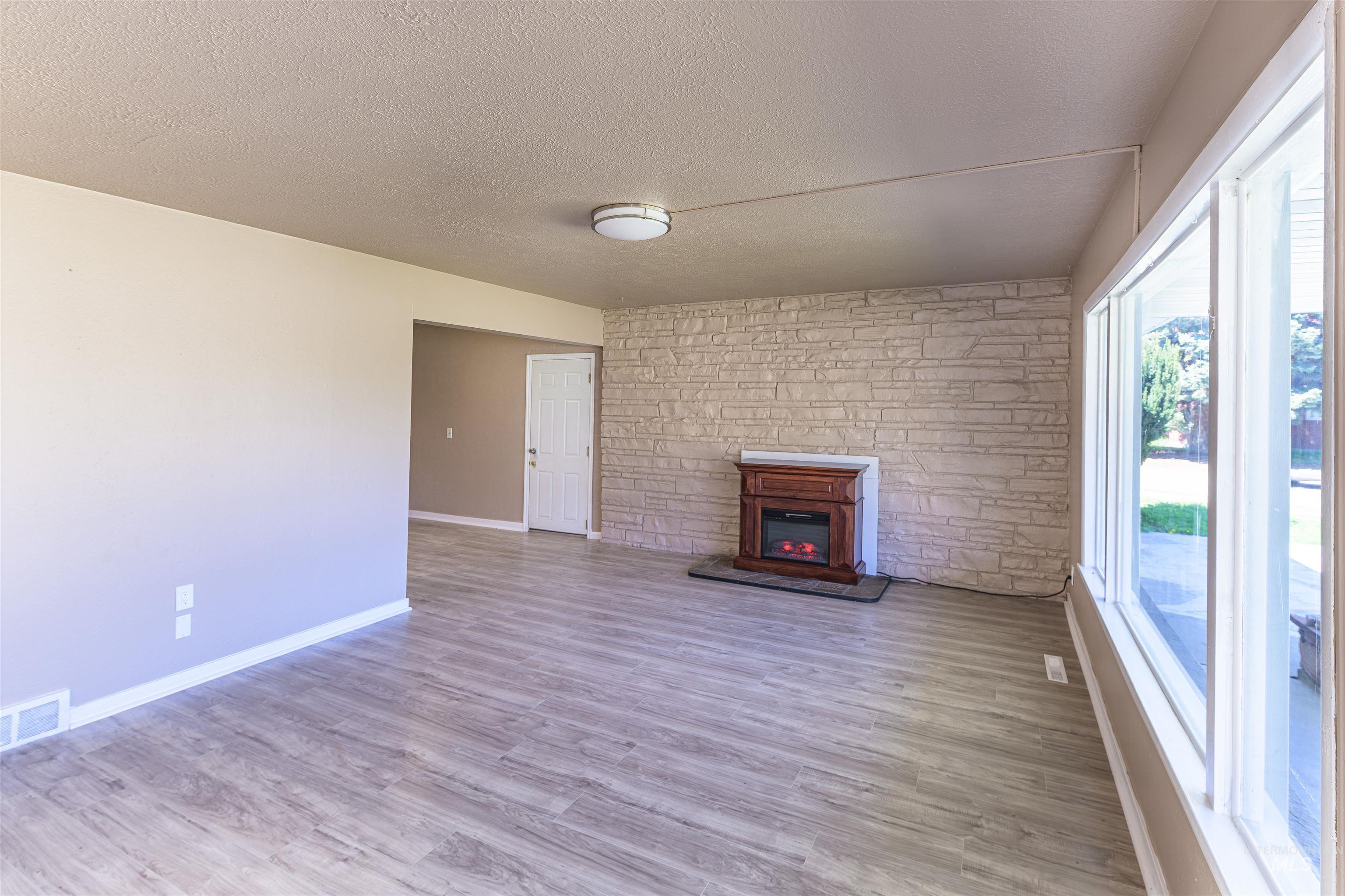 2003 North Cole Road Boise, ID 83704 - Photo 4 of 40 Unfurnished living room featuring a textured ceiling, a glass covered fireplace, light wood-style flooring, and an accent wall
