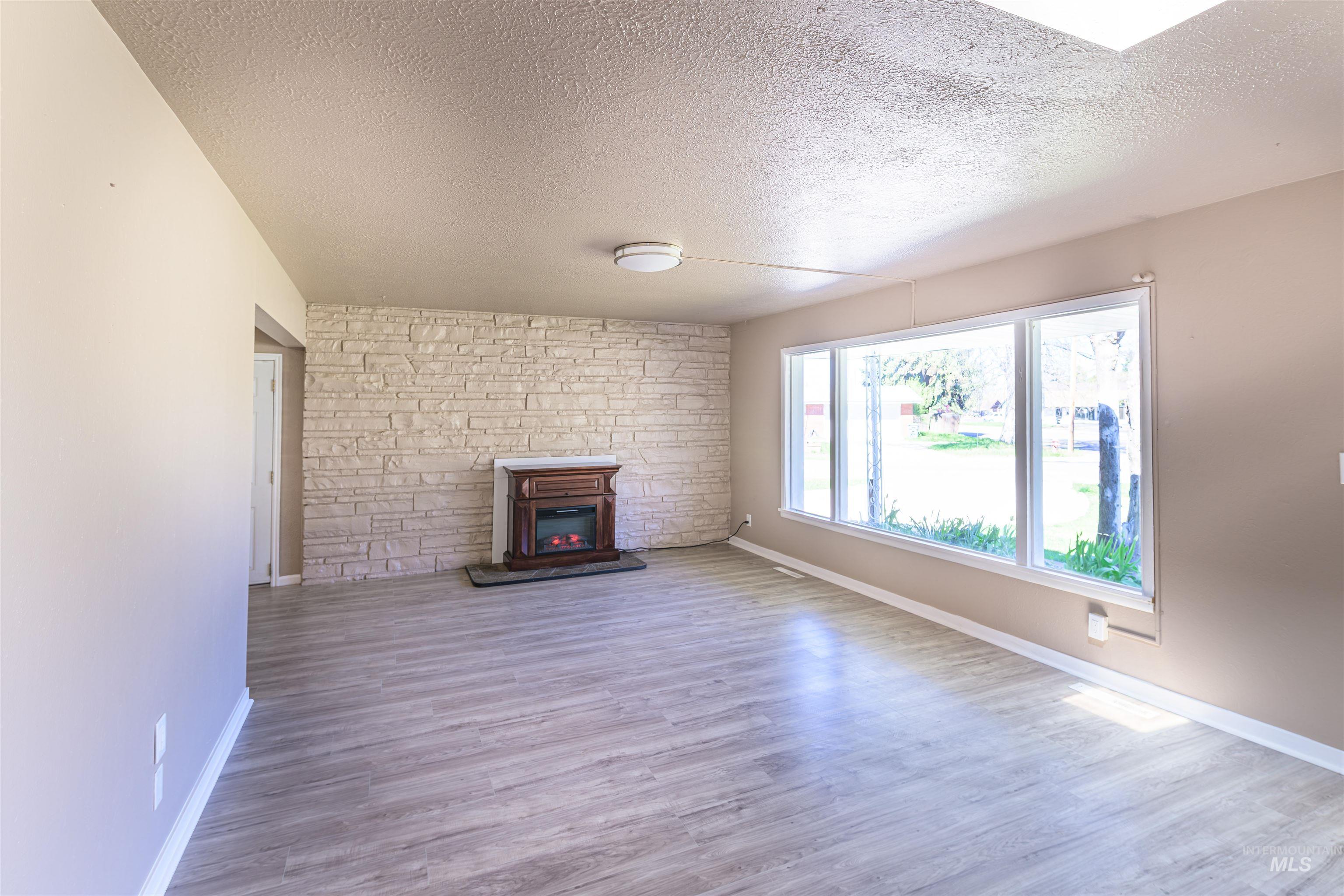 2003 North Cole Road Boise, ID 83704 - Photo 5 of 40 Unfurnished living room featuring light wood-style flooring, a textured ceiling, and a large fireplace