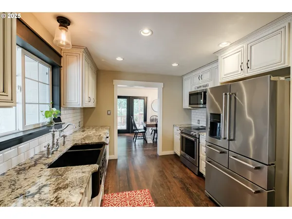 a kitchen with granite countertop a refrigerator a sink dishwasher a stove and white cabinets with wooden floor