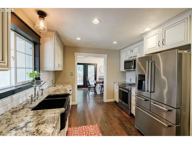 a kitchen with granite countertop a refrigerator a sink dishwasher a stove and white cabinets with wooden floor