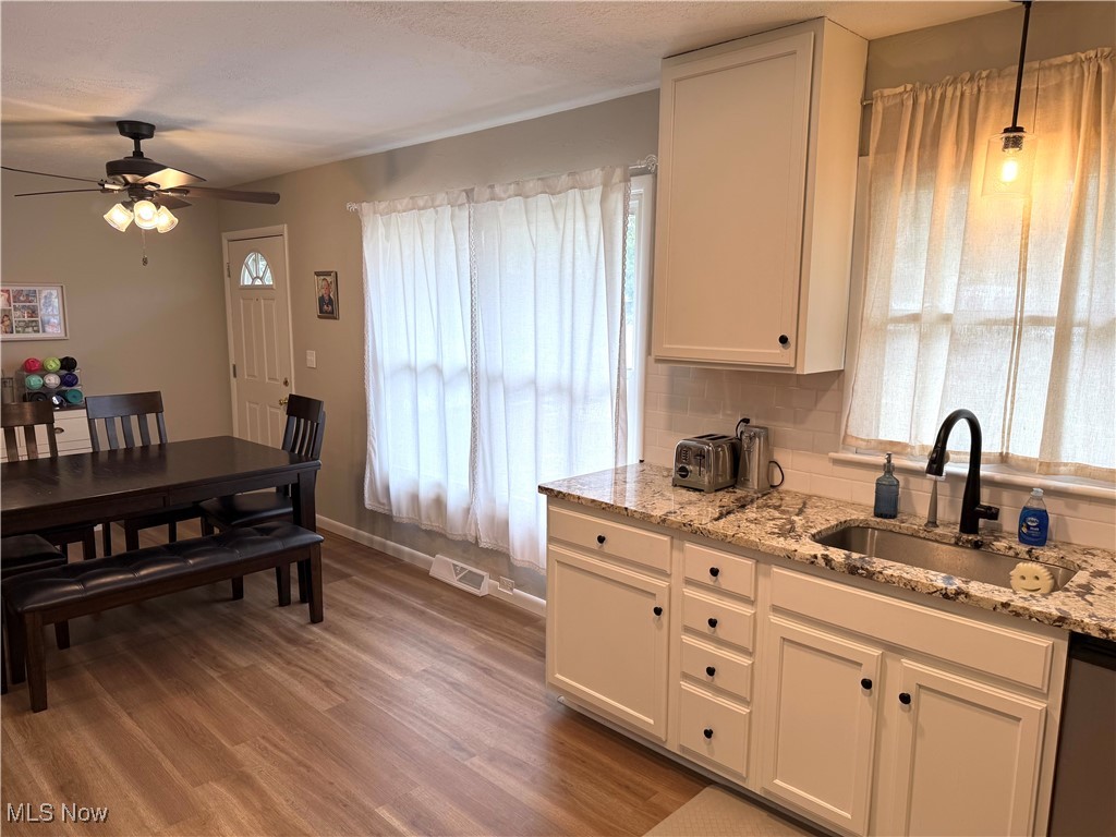 Kitchen featuring sink, light hardwood / wood-style flooring, white cabinetry, tasteful backsplash, and light stone countertops