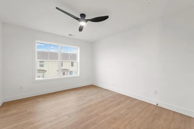 an empty room with wooden floor chandelier fan and windows