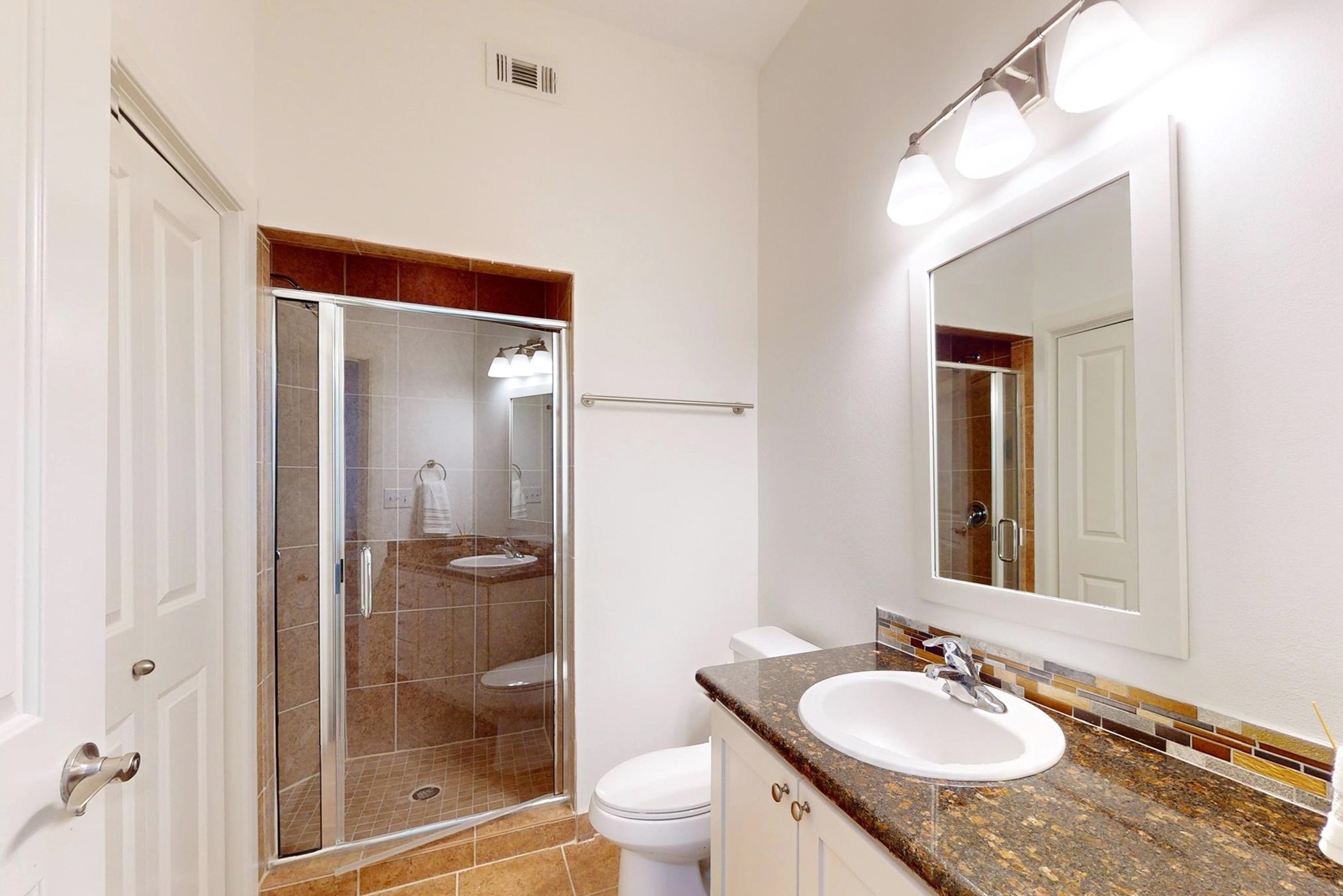 1010 Rosine Street, Unit 29 Houston, TX 77019 - Photo 7 of 16 This modern bathroom features a tiled shower with a glass door, a sleek vanity with a granite countertop, and a large mirror with overhead lighting. The space is bright and well-organized.