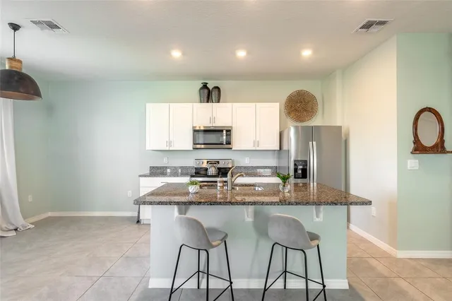 a kitchen with kitchen island granite countertop a stove a sink a refrigerator and white cabinets with wooden floor