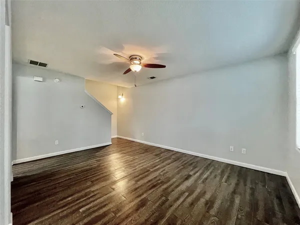 an empty room with wooden floor chandelier fan and windows