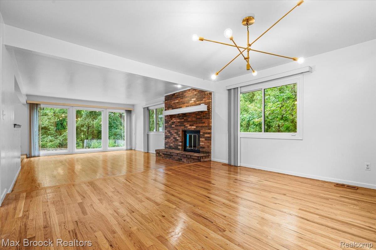 1830 Lone Pine Road Bloomfield Hills, MI 48302 - Photo 16 of 70 Expansive interior featuring wood-finish flooring, a brick-surround fireplace, a modern brass chandelier, and large windows with abundant natural light