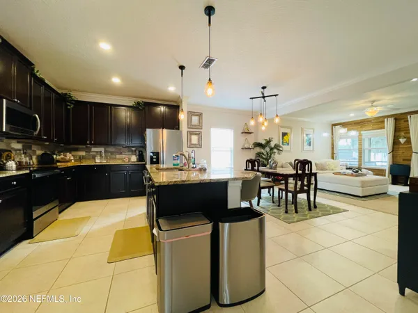 a kitchen with stainless steel appliances kitchen island granite countertop a refrigerator a sink dishwasher a dining table and chairs with wooden floor